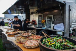 This image shows two members of the Rustic Taps team preparing pizzas in a lineup for guests, as well as a large family style salad for self-service.