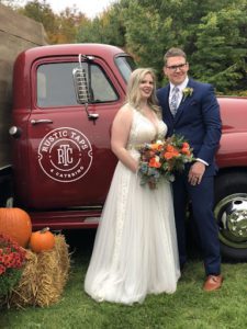 This image features a smiling newlywed couple posing next to a Rustic Taps truck at their reception.