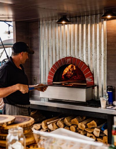 Taking pizza out of the wood fried pizza oven tap truck